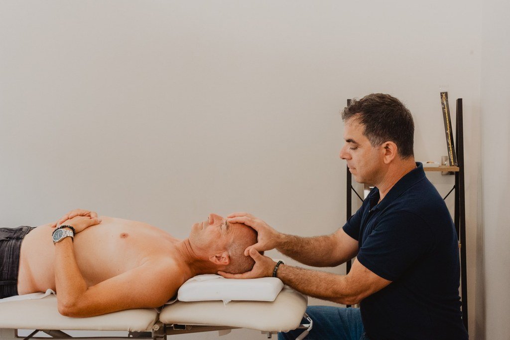 Geste d'ostéopathie crânienne : mains posées sur la tête du patient allongé