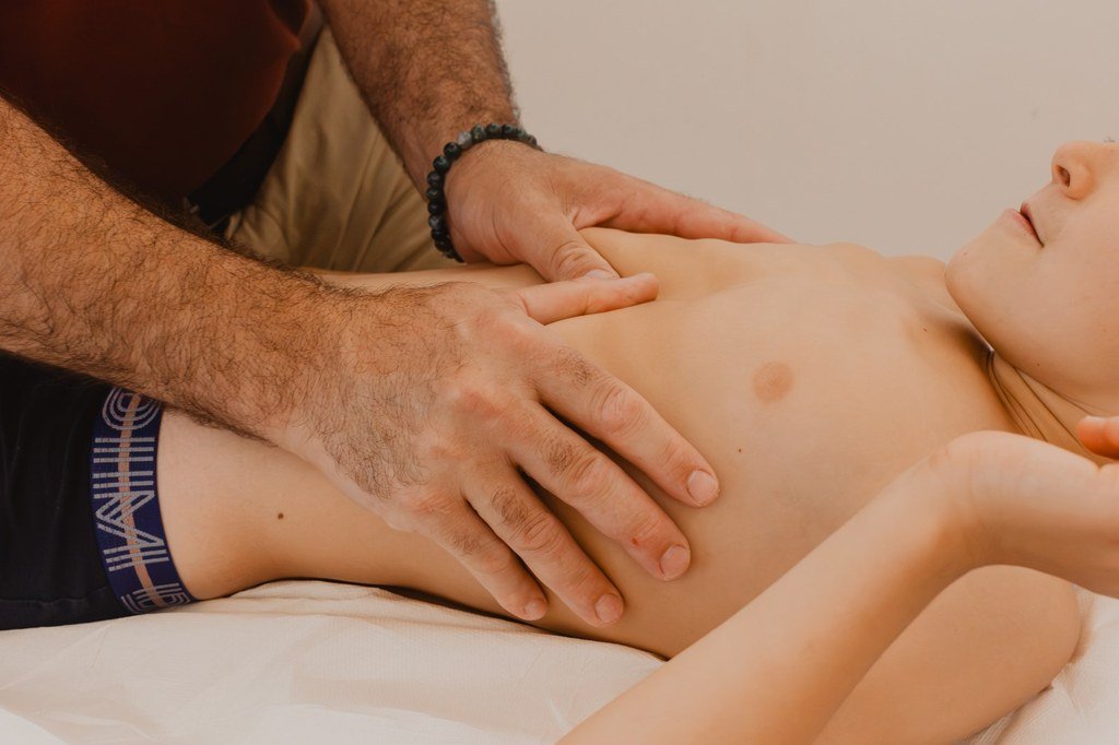 Mains de l'ostéopathe posées sur le ventre d'un enfant allongé : techniques viscérales douces